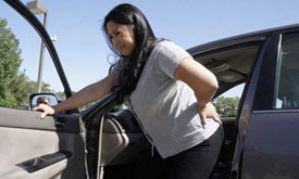 hispanic woman holding back in pain out of car