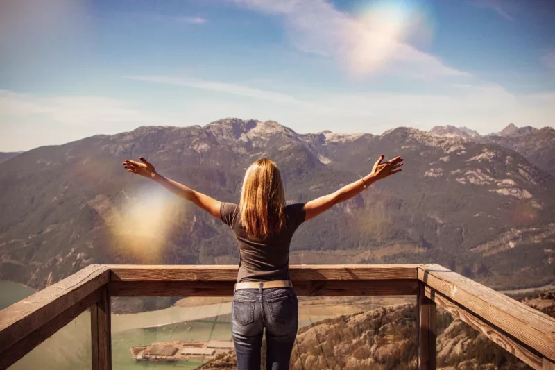 woman with red hair and jeans with hands up near scenic view